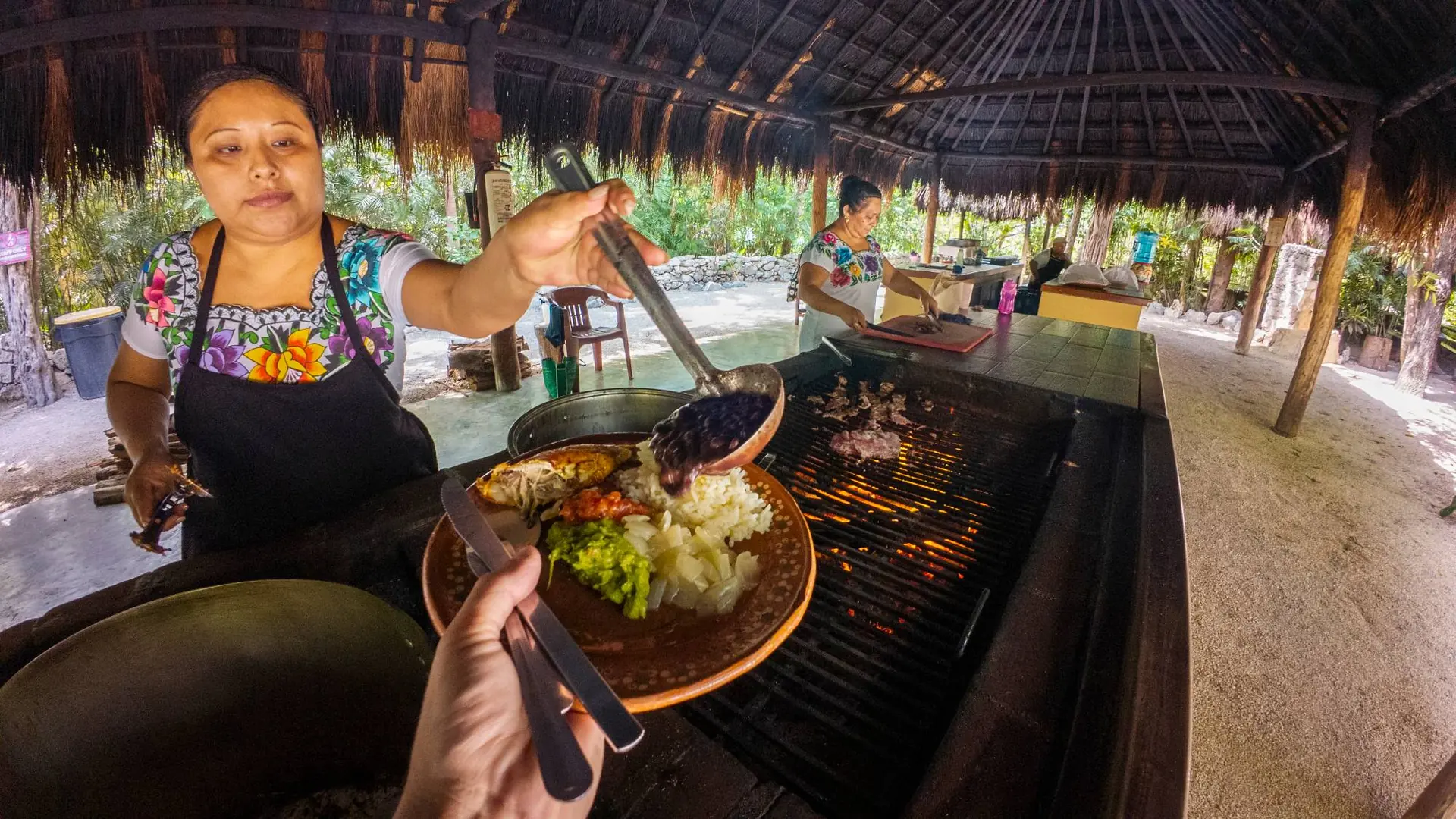 Guest being served black beans and grilled fish at a Maya open-air kitchen